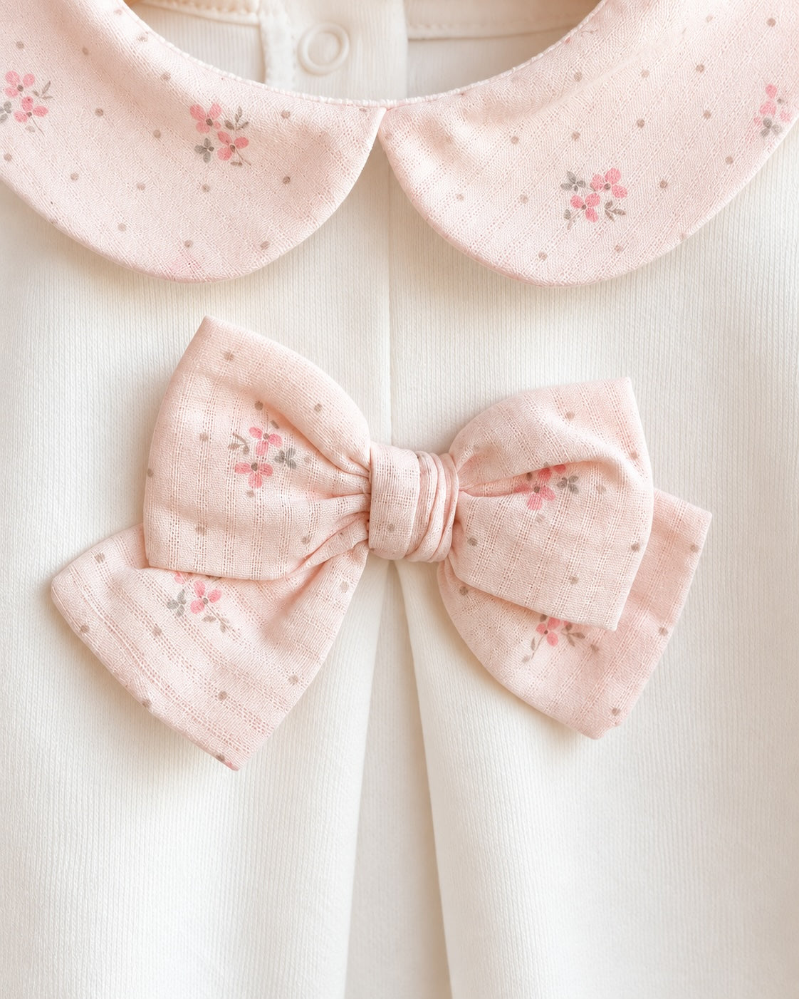 Closeup of white cotton fabric with a double-pink cotton bow and pink floral neck line.