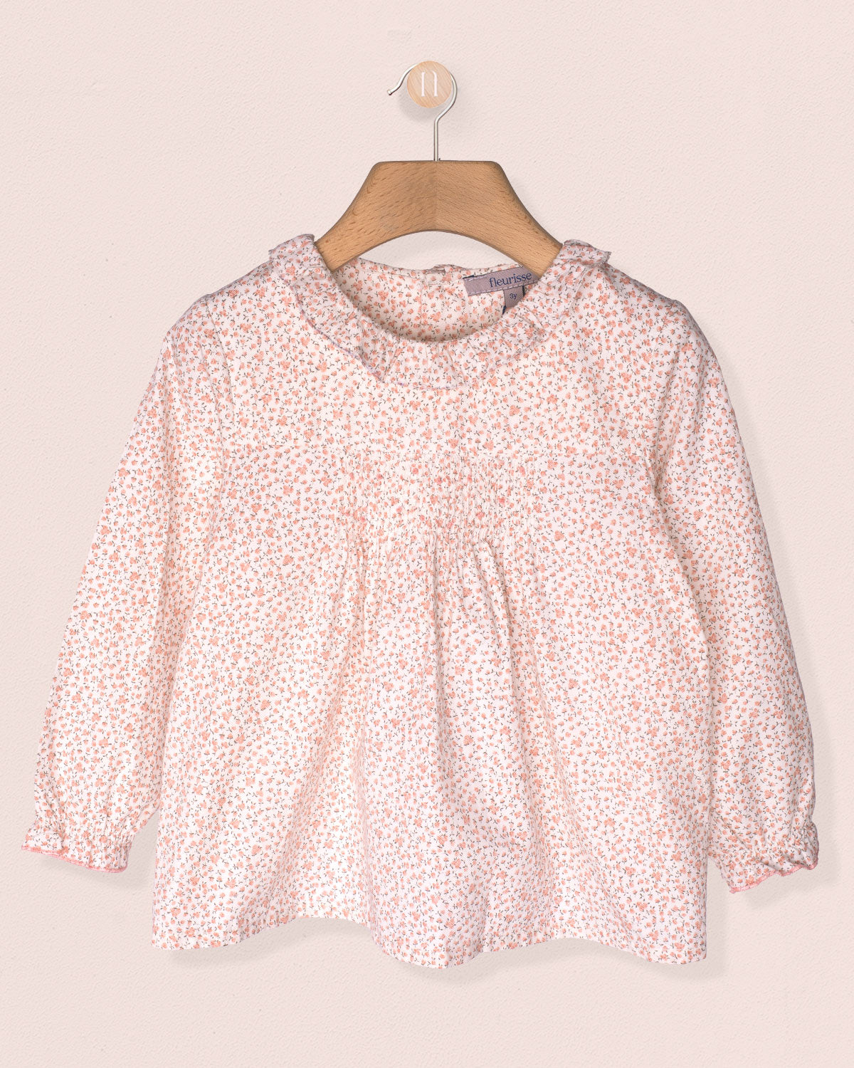 Pink floral blouse on a hanger against a light pink background