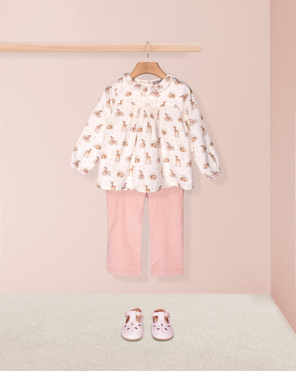Children's outfit with a patterned top and pink pants on a hanger against a pink background.