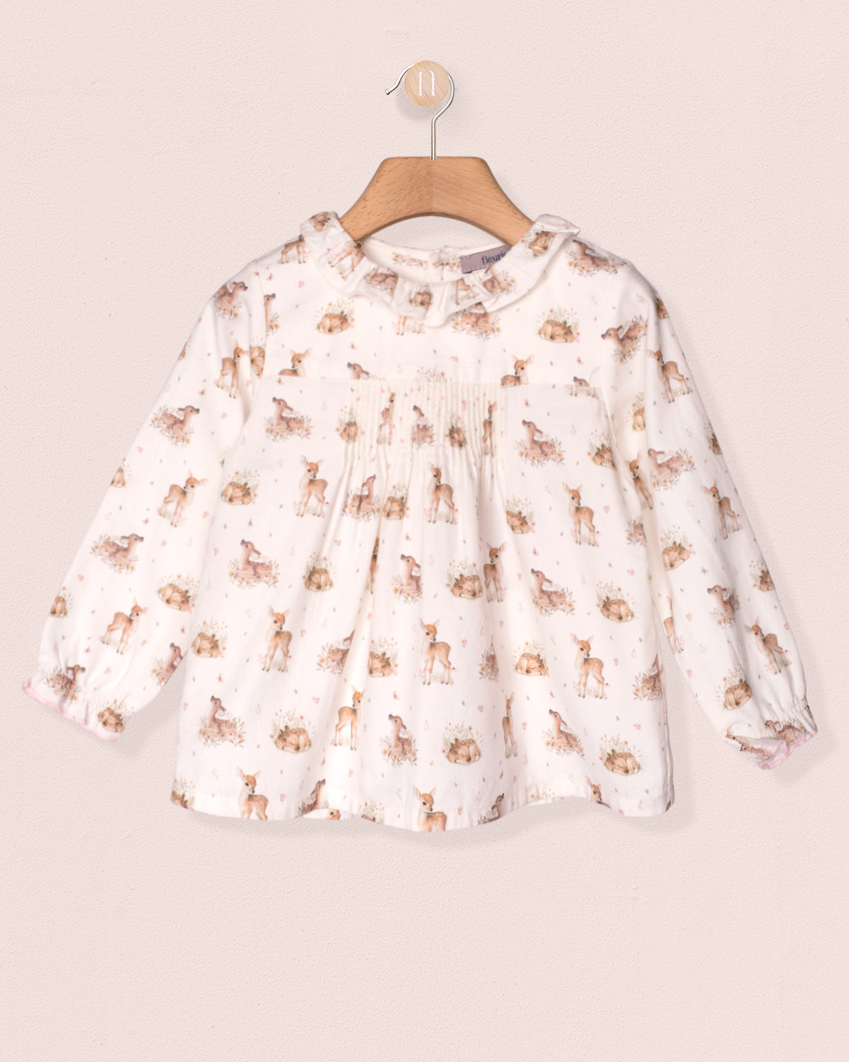 White blouse with animal print on a wooden hanger against a beige background