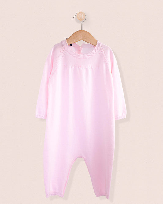Pink onesie on a hanger against a beige background