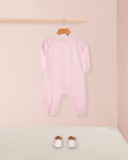 Pink baby onesie hanging on a wooden hanger against a light pink wall.