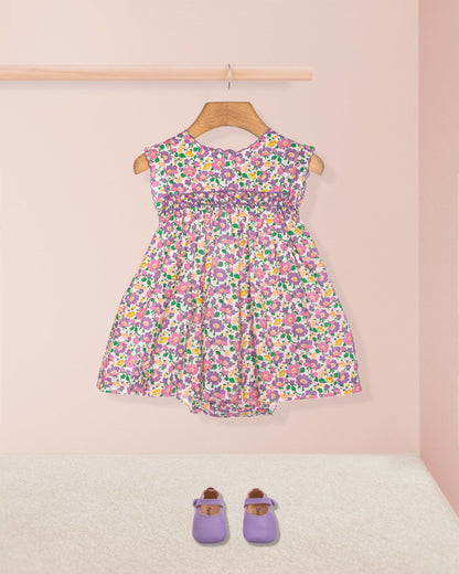 Floral dress on a hanger with purple shoes on the floor against a pink wall.
