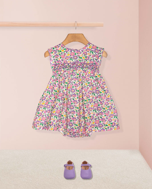 Floral dress on a hanger with purple shoes on the floor against a pink wall.