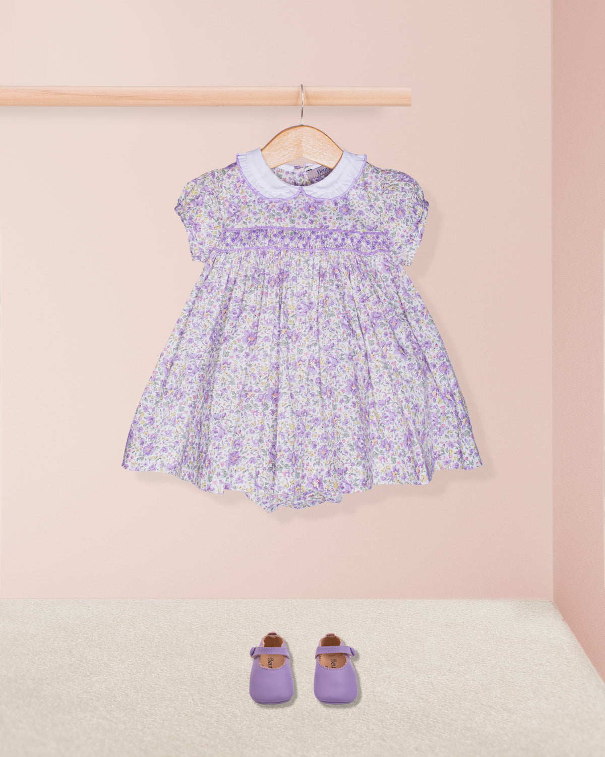 Lavender floral dress on a hanger with matching shoes on the floor against a pink background