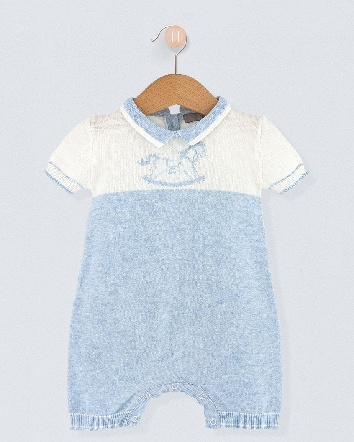 Baby romper with white top and blue knitted bottom on a hanger against a light gray background