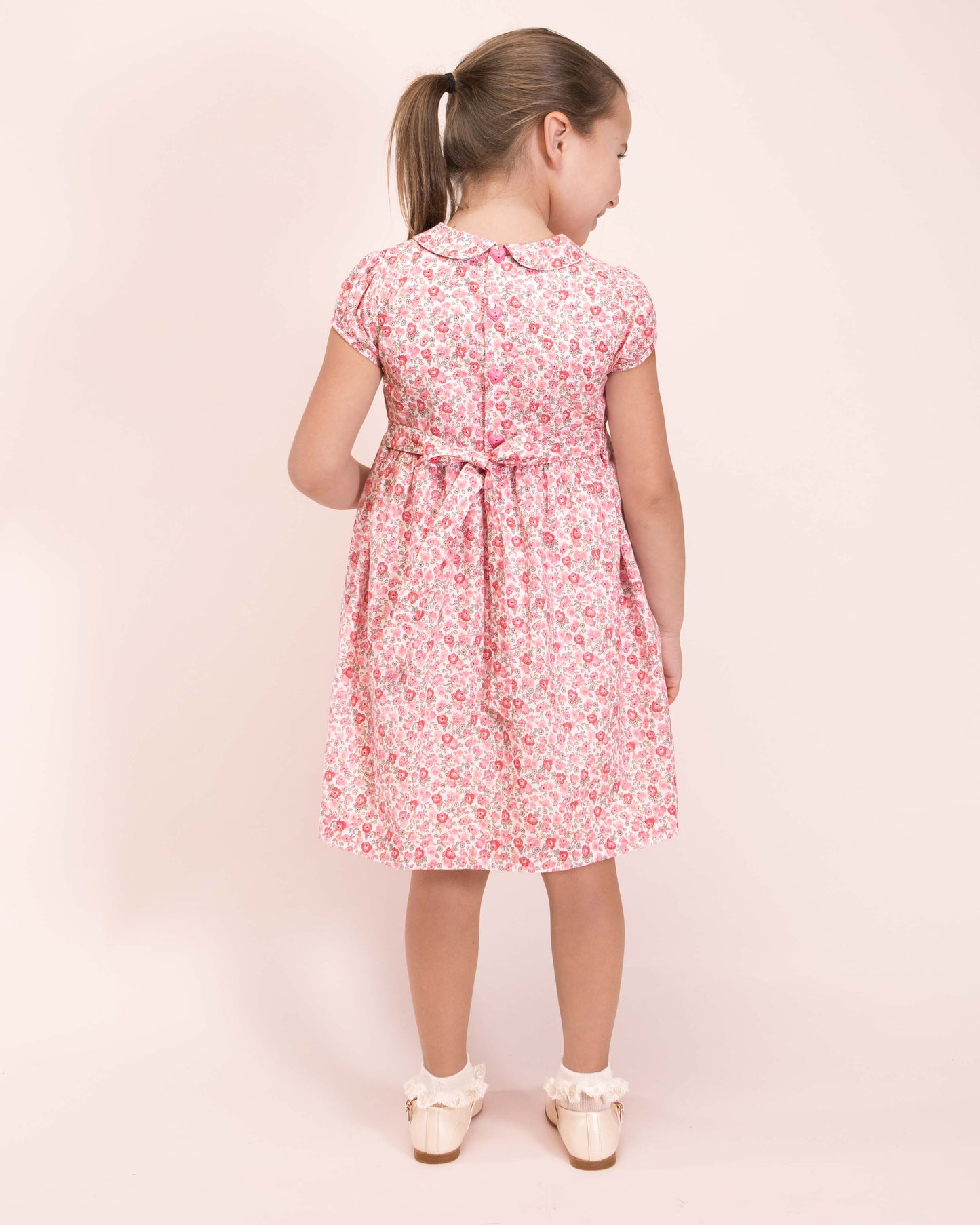 Girl wearing Violette French Blossom Pink Smocked Dress with Cream Shoes and Ruffle Socks showing the back of the dress 