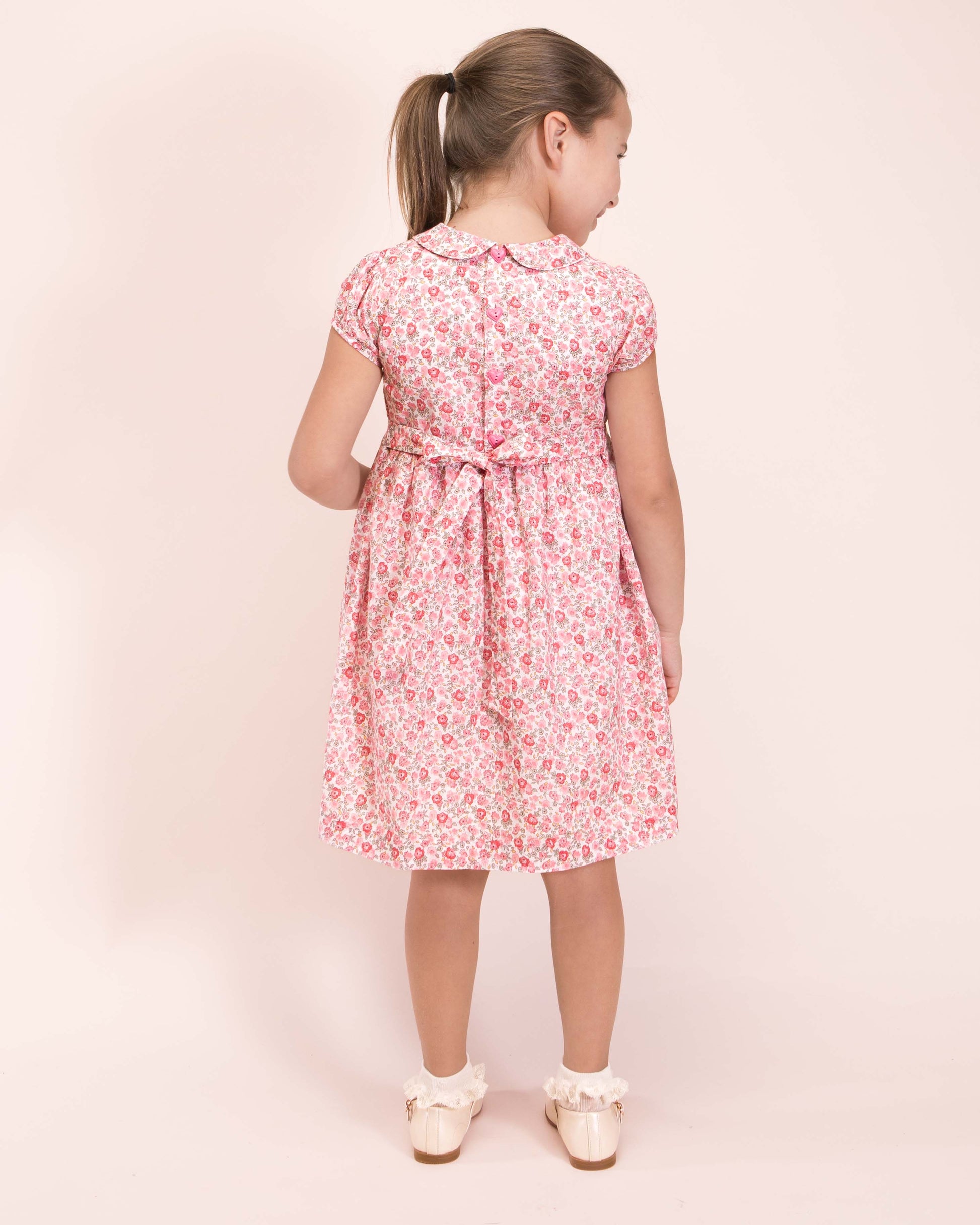 Girl wearing Violette French Blossom Pink Smocked Dress with Cream Shoes and Ruffle Socks showing the back of the dress 