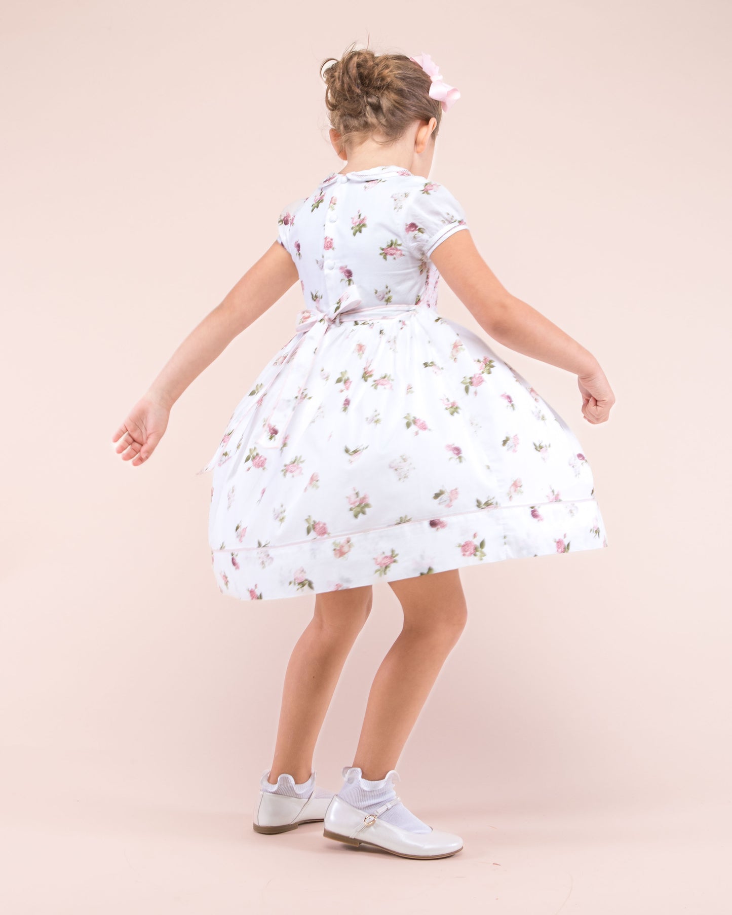 Girl twirling wearing Emma Delicate Blush Rose Smock dress showing the back and the side of the dress