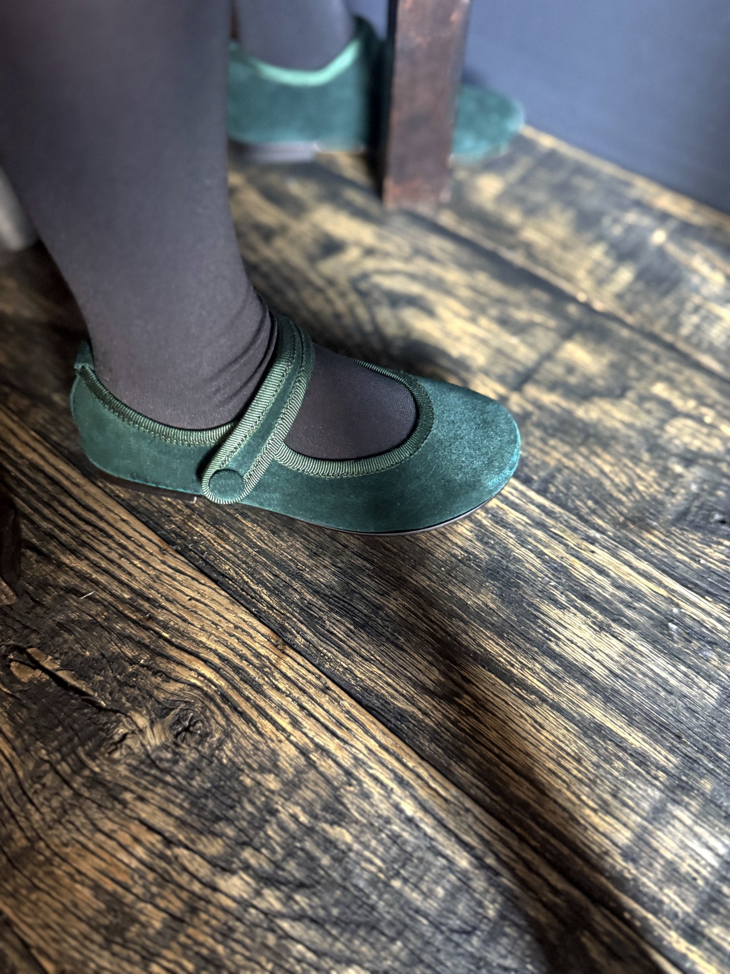 Green suede shoes on a girl worn with black tights on a wooden floor.