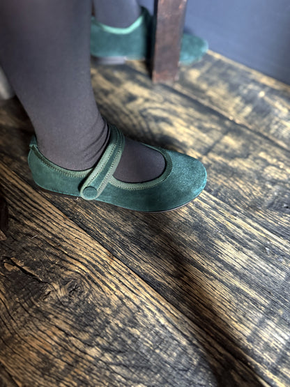 Green suede shoes on a girl worn with black tights on a wooden floor.