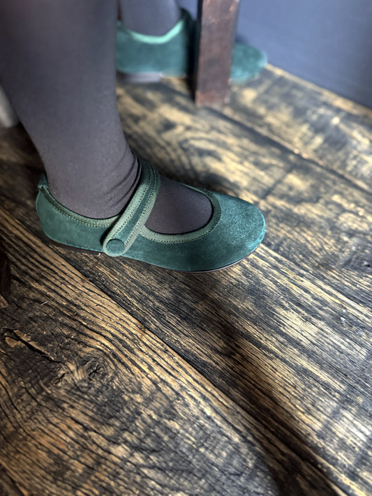 Green suede shoes on a girl worn with black tights on a wooden floor.