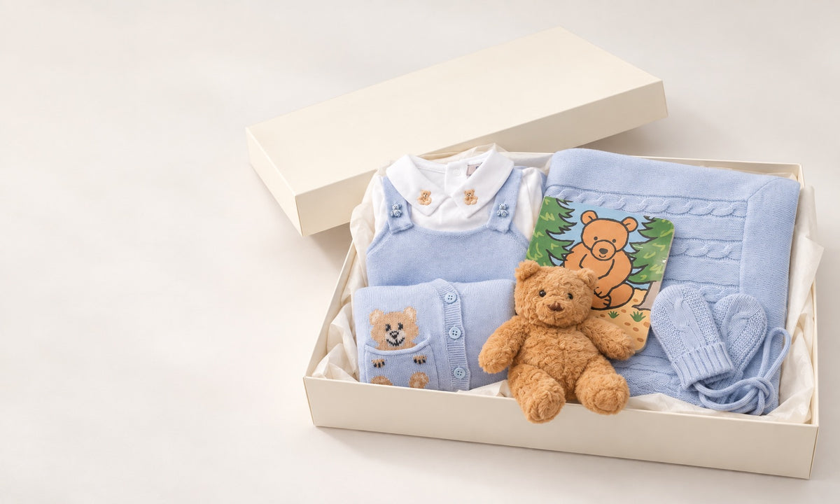 gift box with baby blue sweaters, mittens, a plush baby bear toy and light blue cashmere overalls