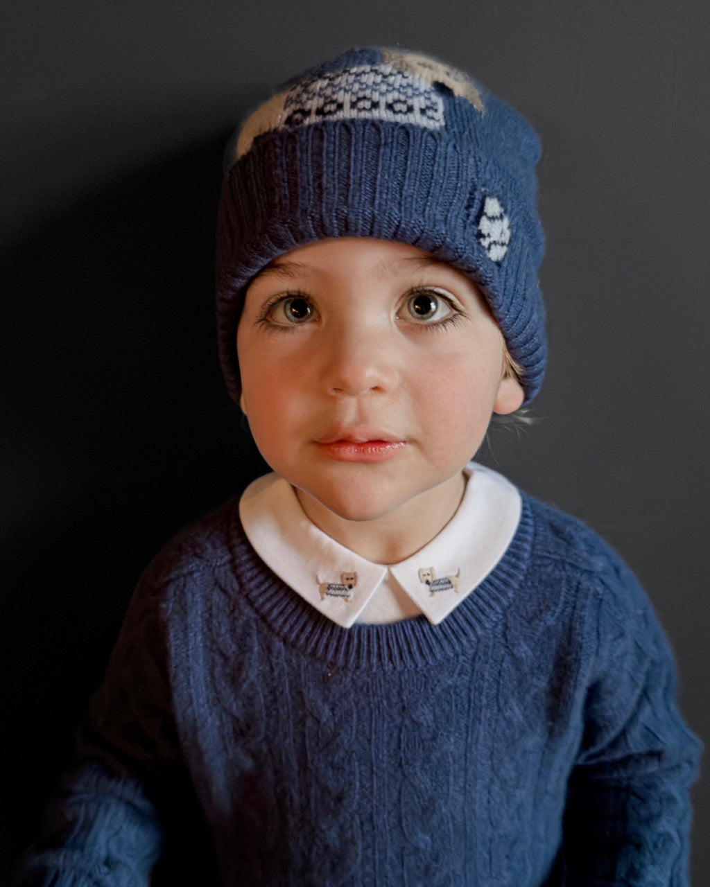Child wearing a blue knitted hat and sweater against a dark background