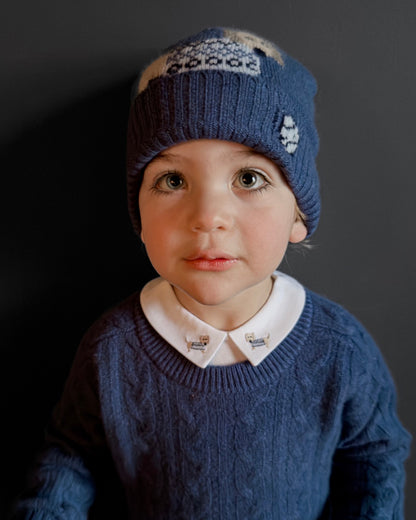 Child wearing a blue knitted hat and sweater against a dark background
