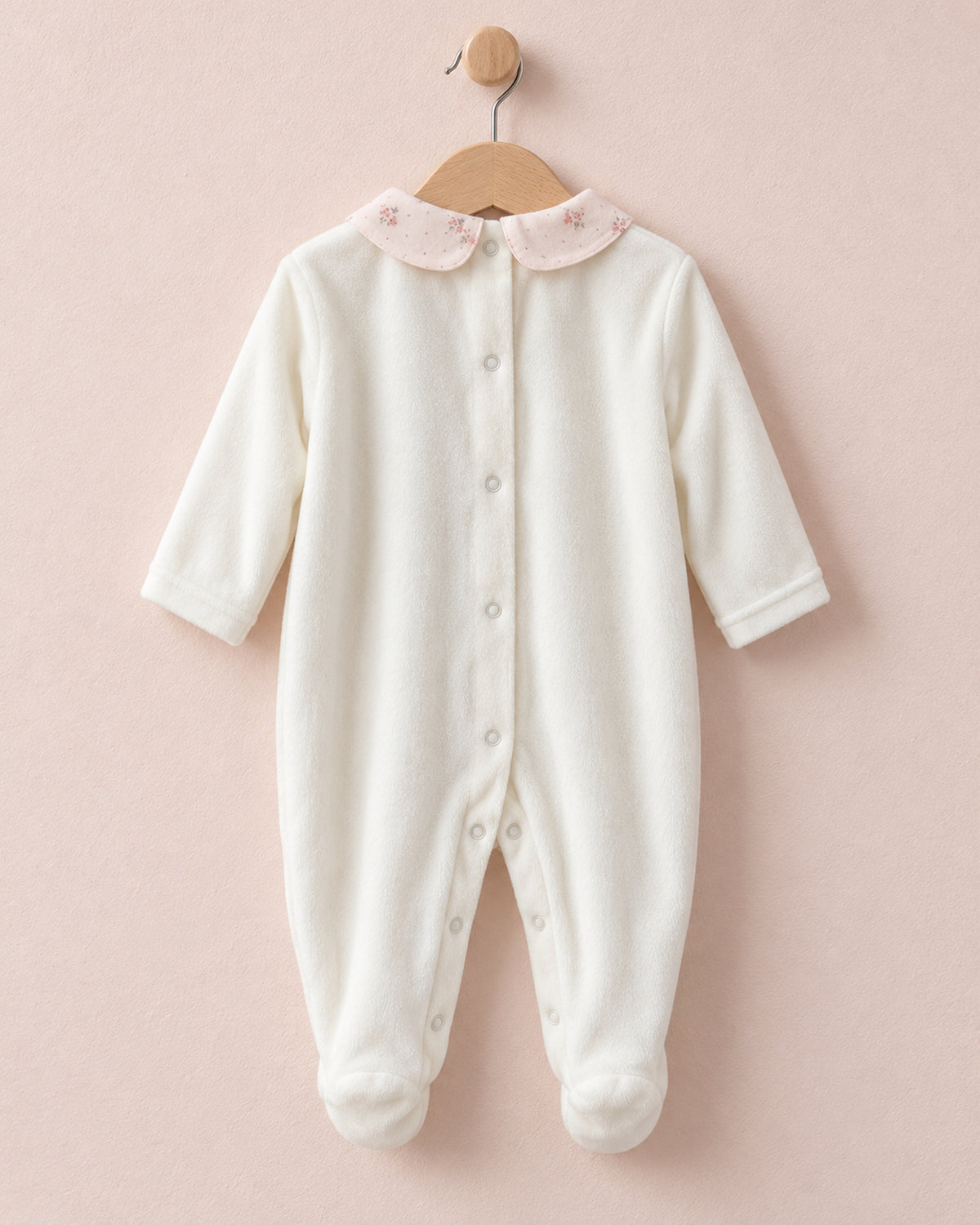 Back of white velour baby onesie hanging from wooden hanger, with light pink floral motif collars.