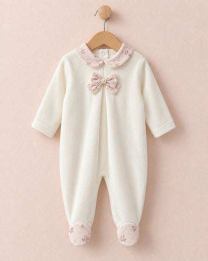 Front of white velour baby onesie hanging from wooden hanger, with light pink bows in center of chest, and pink floral motif collars and feet.