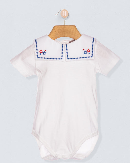 White baby romper with embroidered collar on a wooden hanger against a light gray background