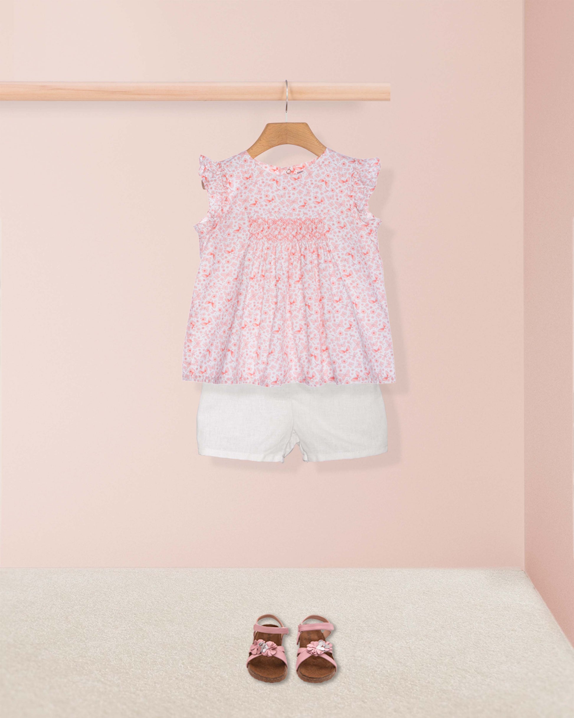 Children's outfit with floral top and white shorts on a pink background
