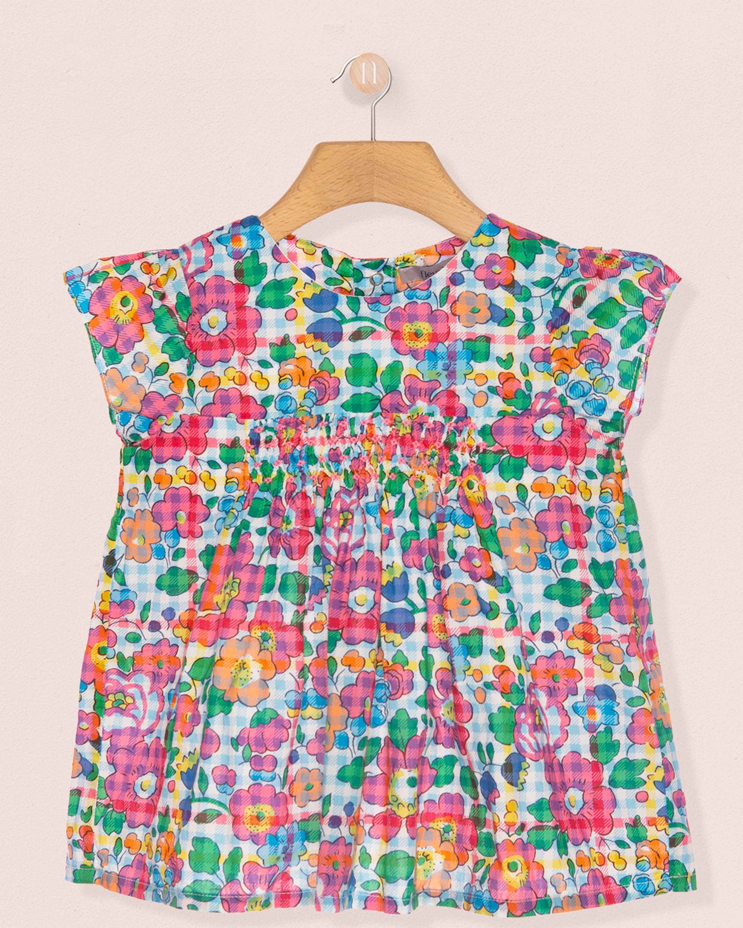 Colorful floral dress on a hanger against a beige background
