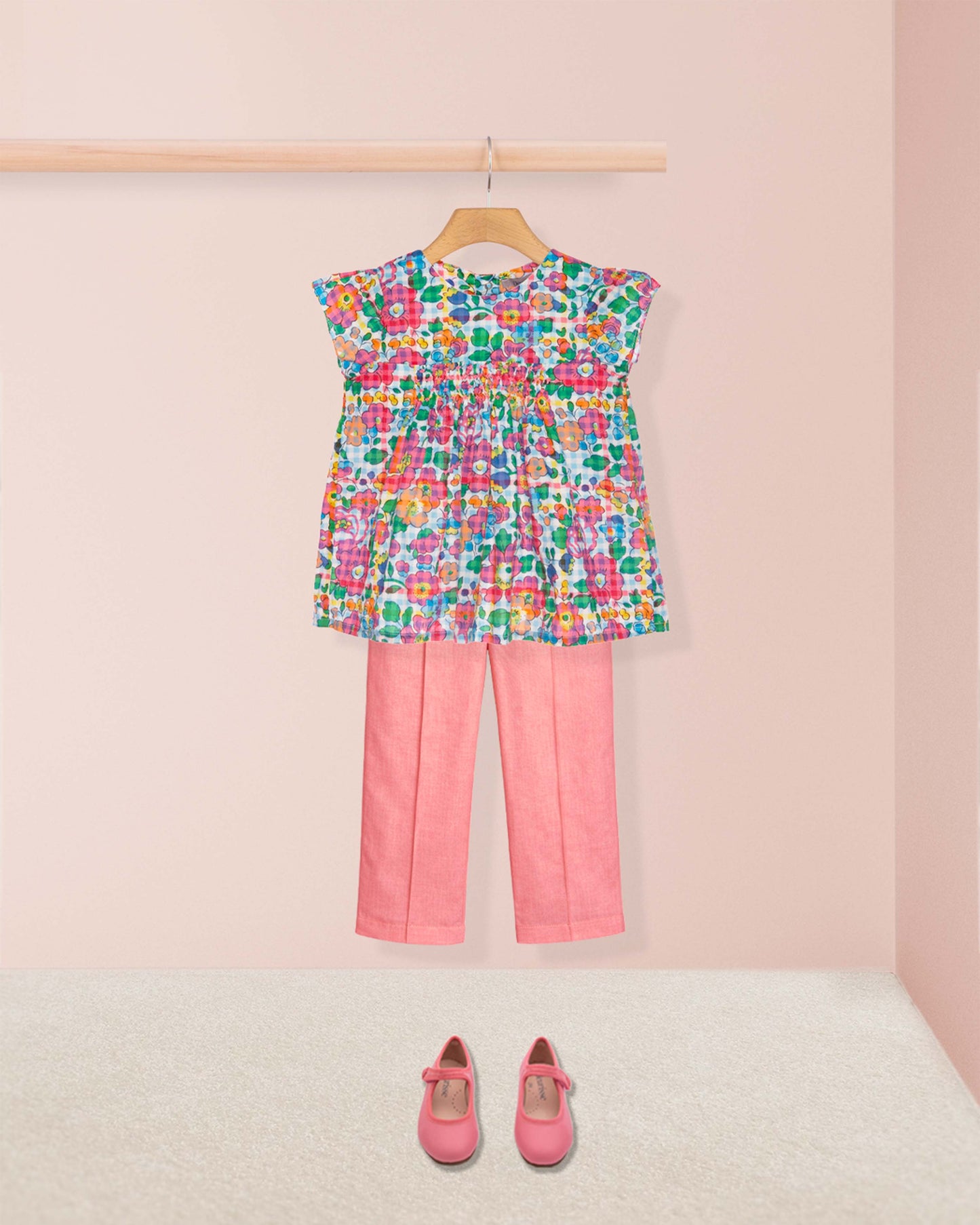 Colorful floral top and pink pants with shoes on a light pink background