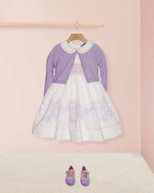 Children's outfit with a white dress and purple cardigan on a pink background