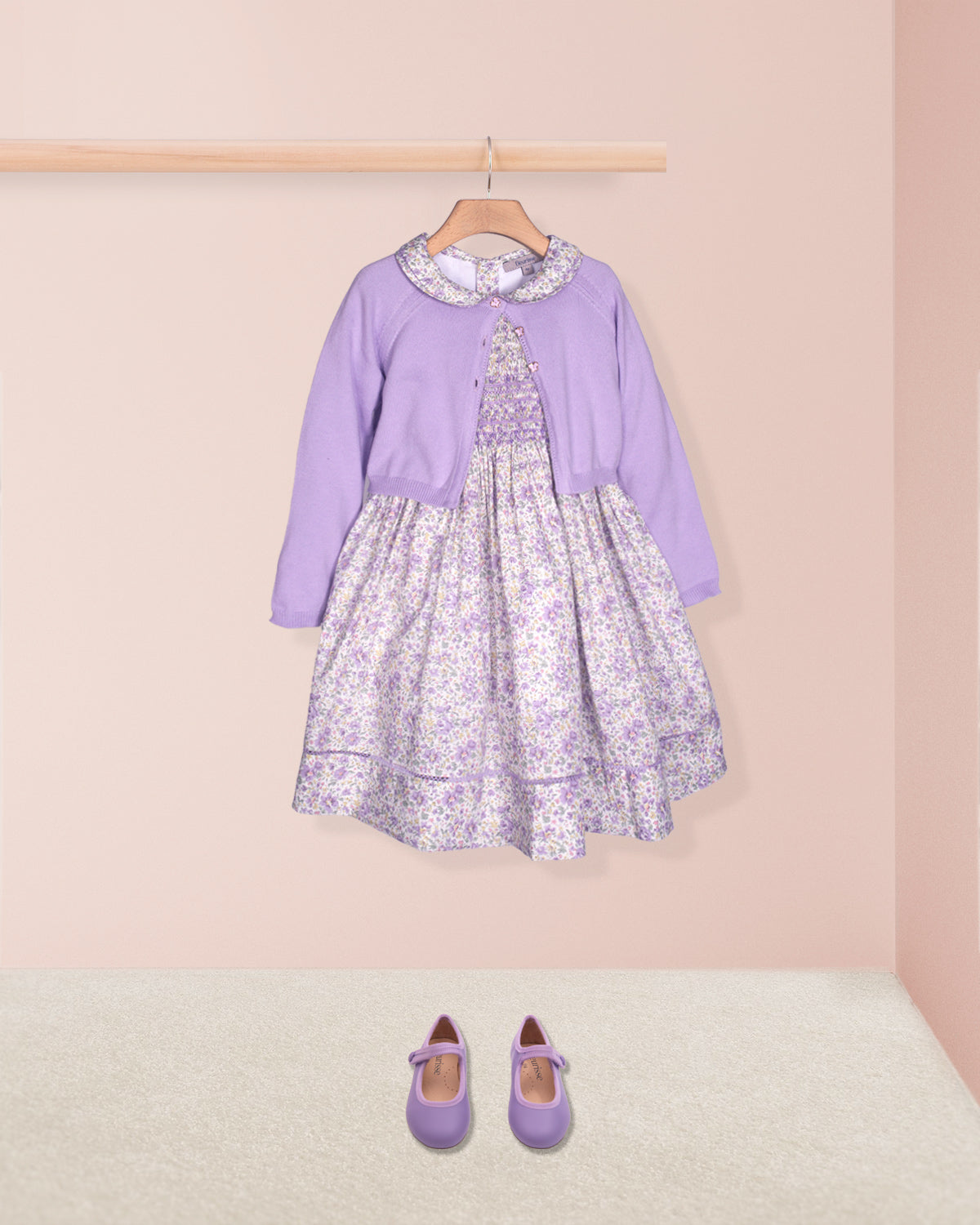 Lavender dress with floral pattern on a hanger against a pink wall.