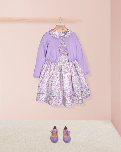 Lavender dress with floral pattern on a hanger against a pink wall.