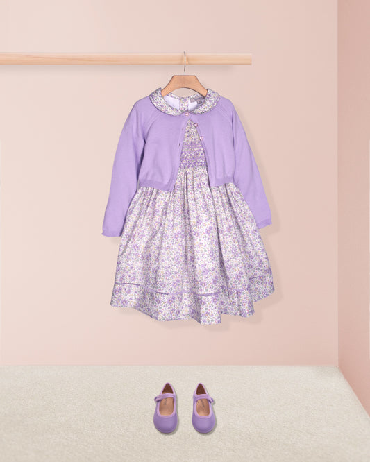 Lavender dress with floral pattern on a hanger against a pink wall.