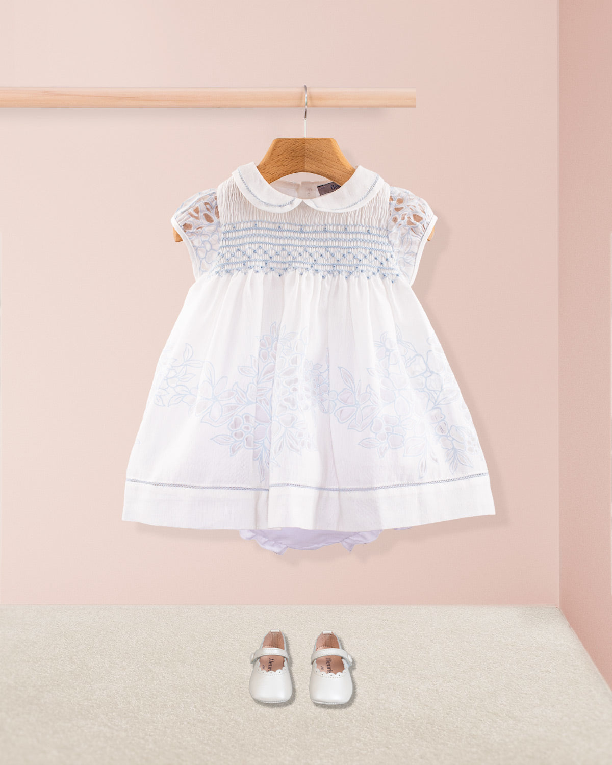 Baby Emmy Doppia Blue Smock Set styled with white leather baby shoes and matching diaper cover, displayed against a pale pink background