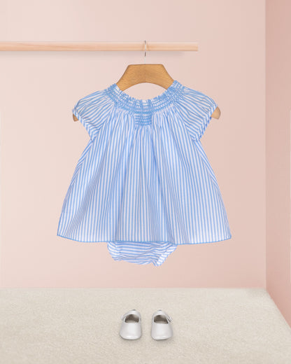 Blue and white striped baby dress on a hanger with white shoes on a pink background