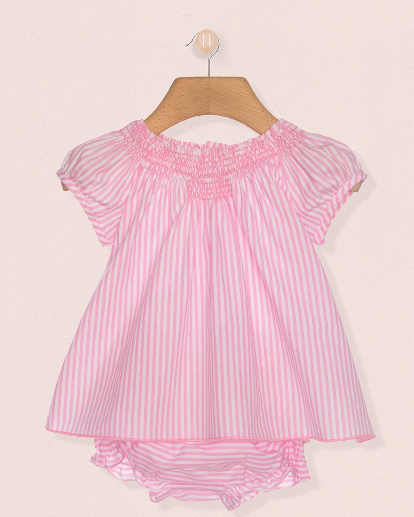 Pink and white striped baby dress on a hanger against a beige background