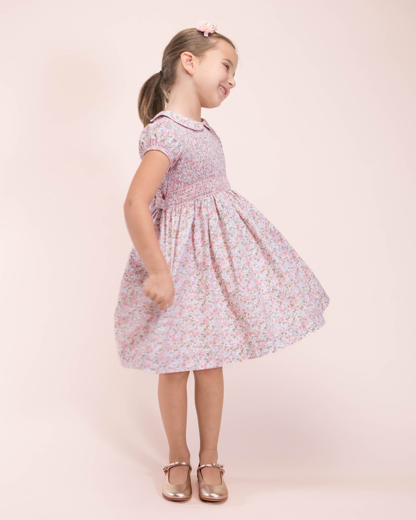 Girl twirling in pink floral smocked dress styled with metallic shoes.