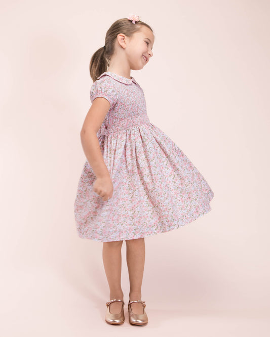 Girl twirling in pink floral smocked dress styled with metallic shoes.
