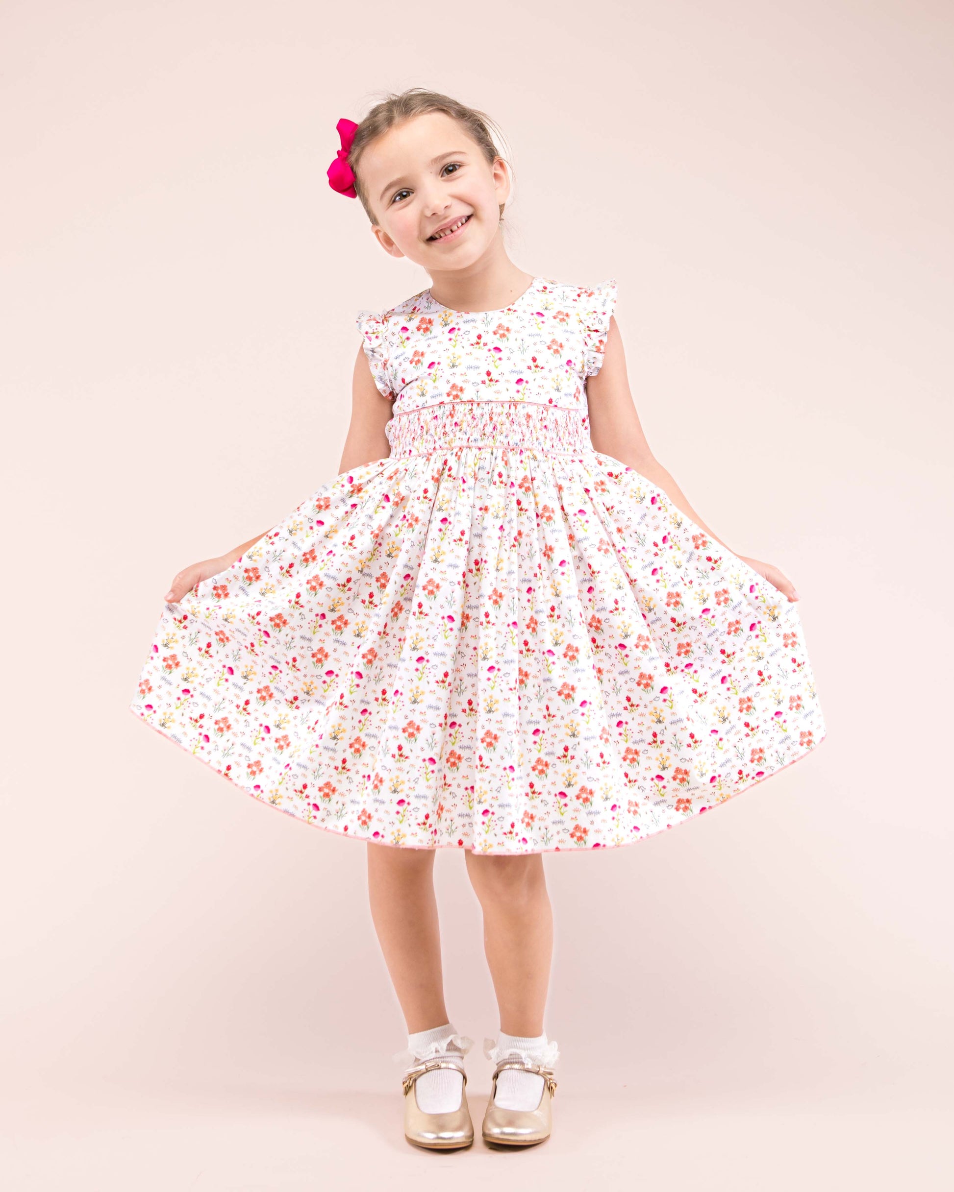 Girl wearing Bonnie Happy Garden Smocked Dress with gold shoes and pink hair bow showing the front of the dress