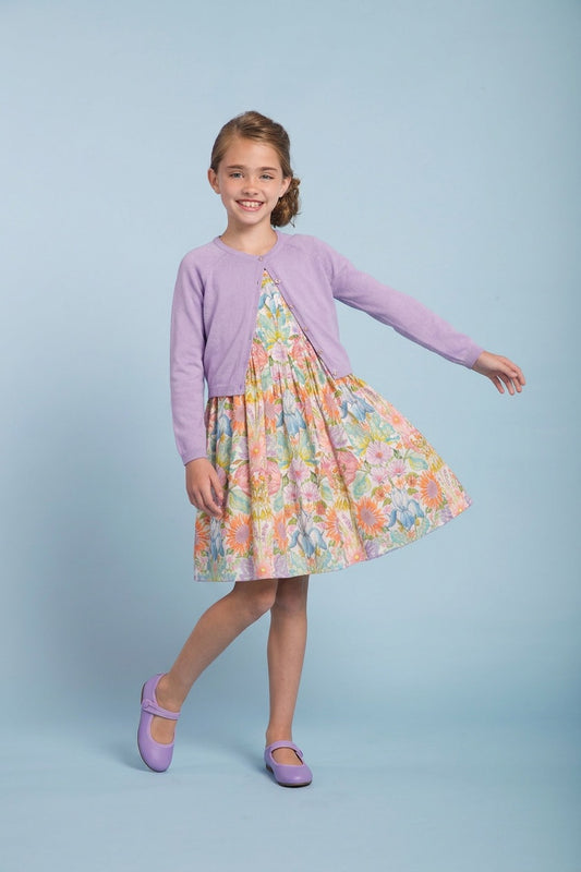 Young girl wearing a floral dress and purple cardigan on a light blue background