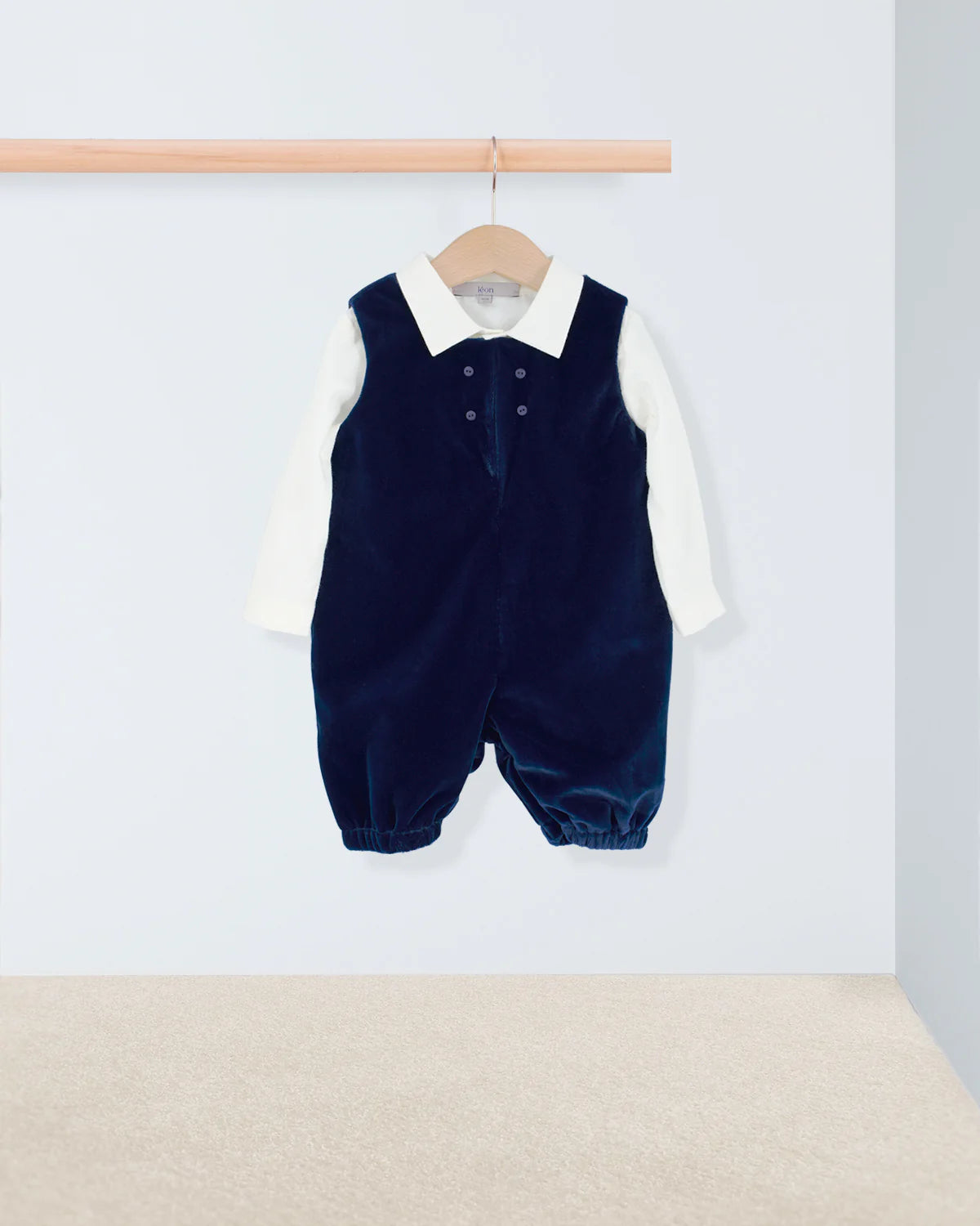 Navy blue baby romper with white shirt on a hanger against a light background