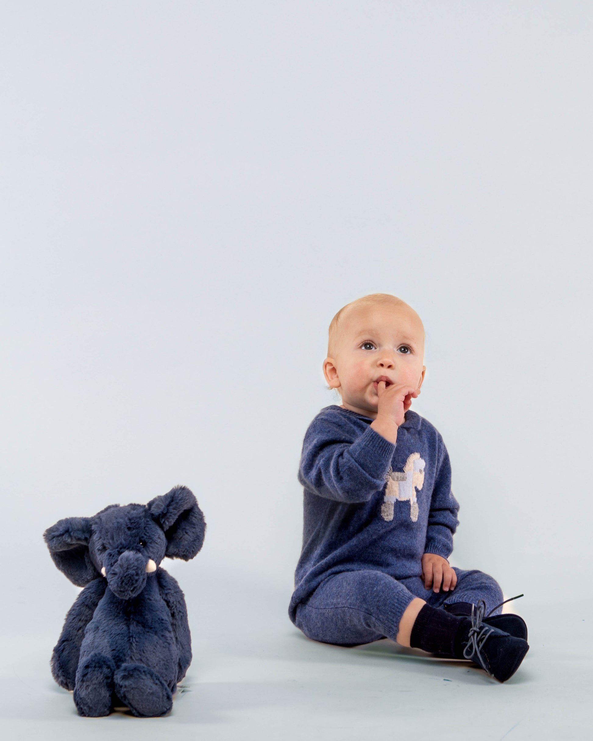 Baby boy model wearing the Logan Jean Cashmere Romper sitting down, showing the front of the romper