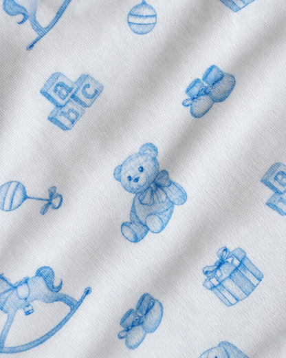 White fabric with a blue repeating pattern of baby-themed illustrations including a teddy bear, blocks, booties, a rattle, a rocking horse, and a gift box.