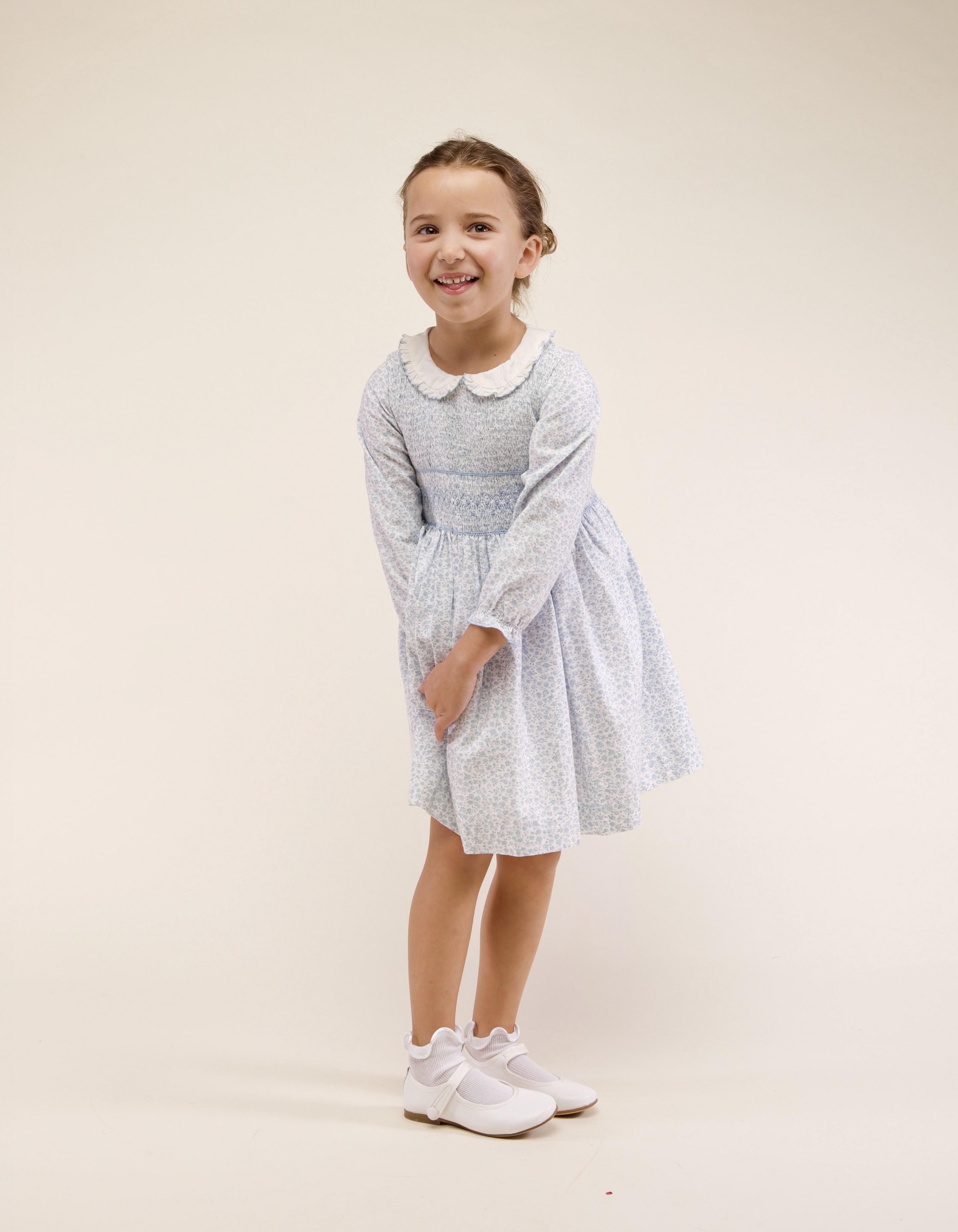 Young girl wearing a light blue checkered dress with a white collar on a beige background