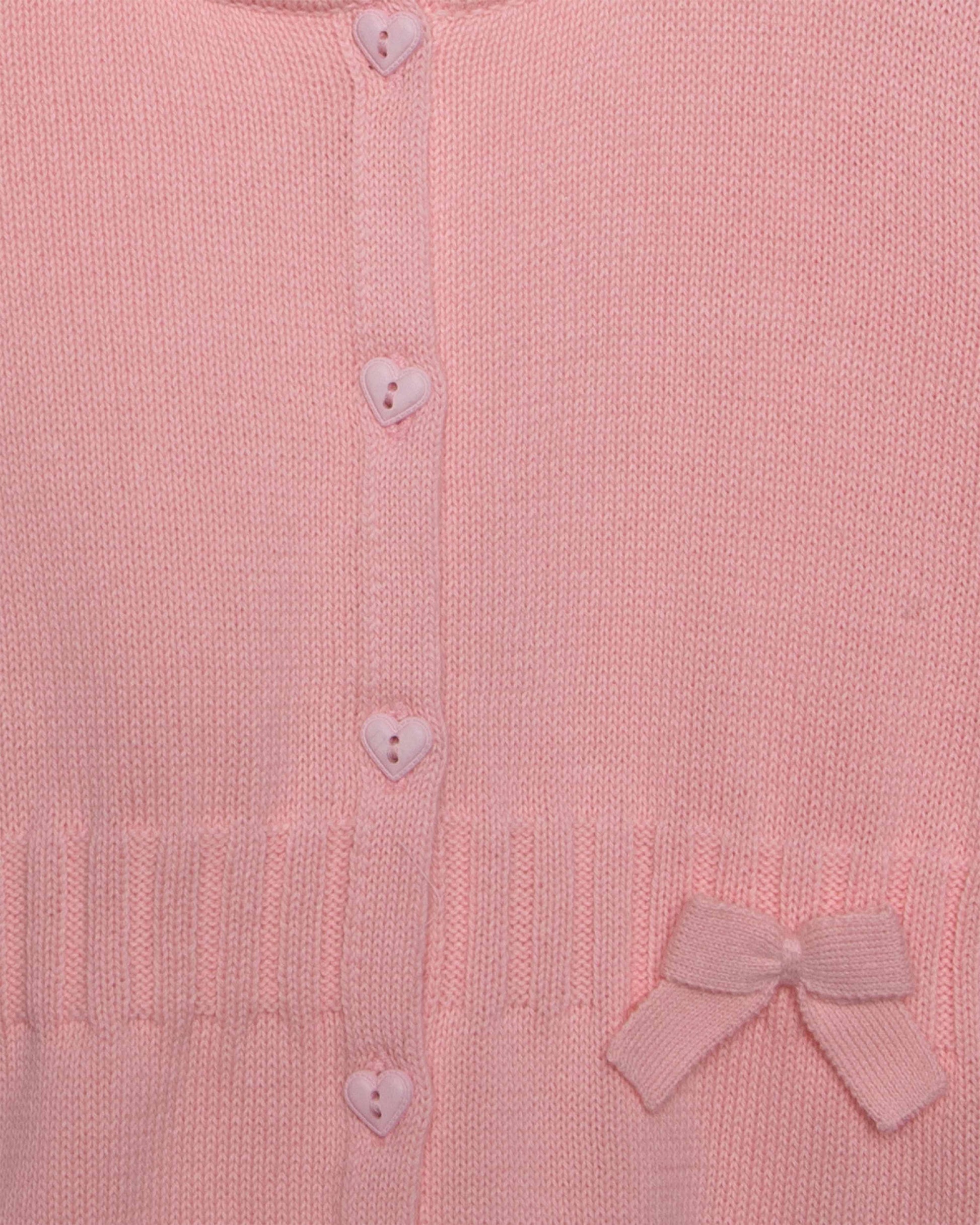 Close-up of a pink knitted cardigan with heart buttons and a bow detail.