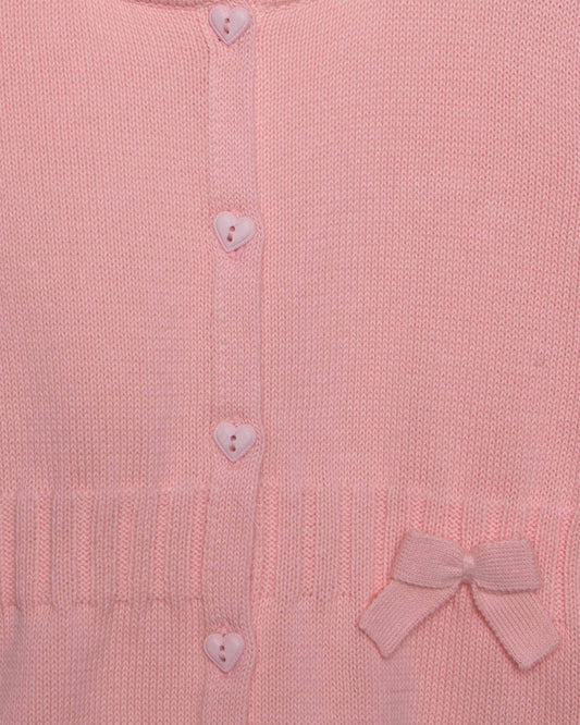 Close-up of a pink knitted cardigan with heart buttons and a bow detail.
