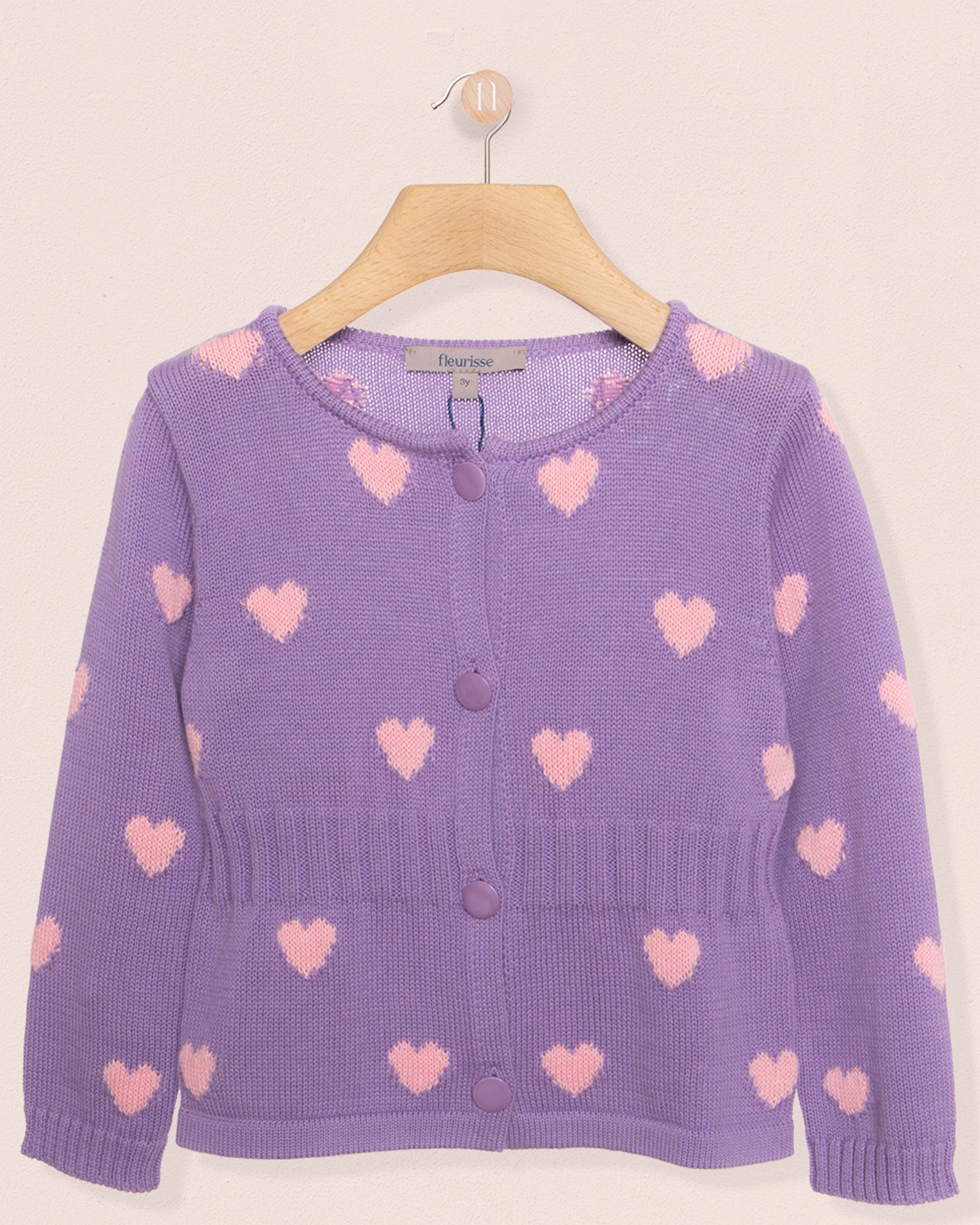 Purple cardigan with pink heart patterns on a beige background
