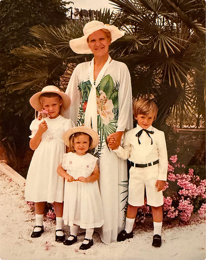 Vintage photo of a woman with three children outdoors, surrounded by plants and flowers.