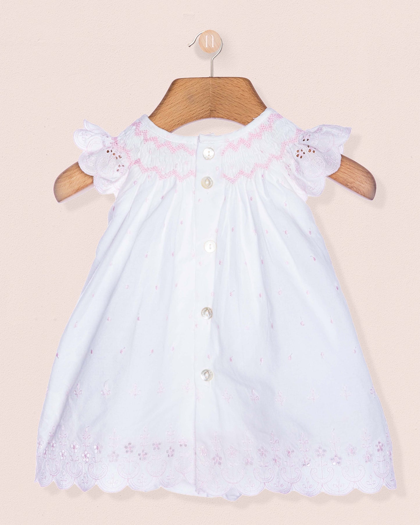White baby dress with pink embroidery on a beige background