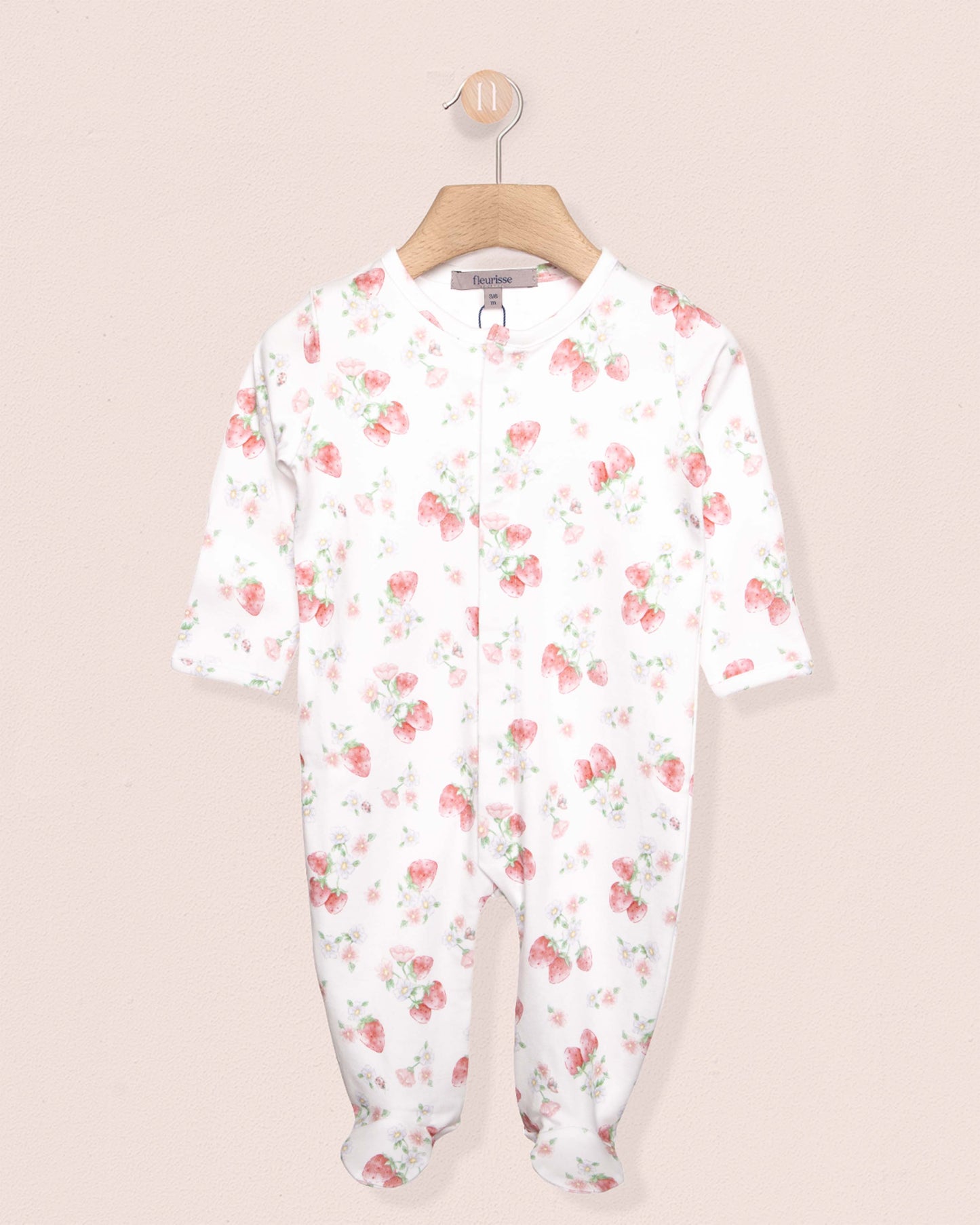 white onesie stretchie for babies with red strawberry designs, on a hanger against a peach background