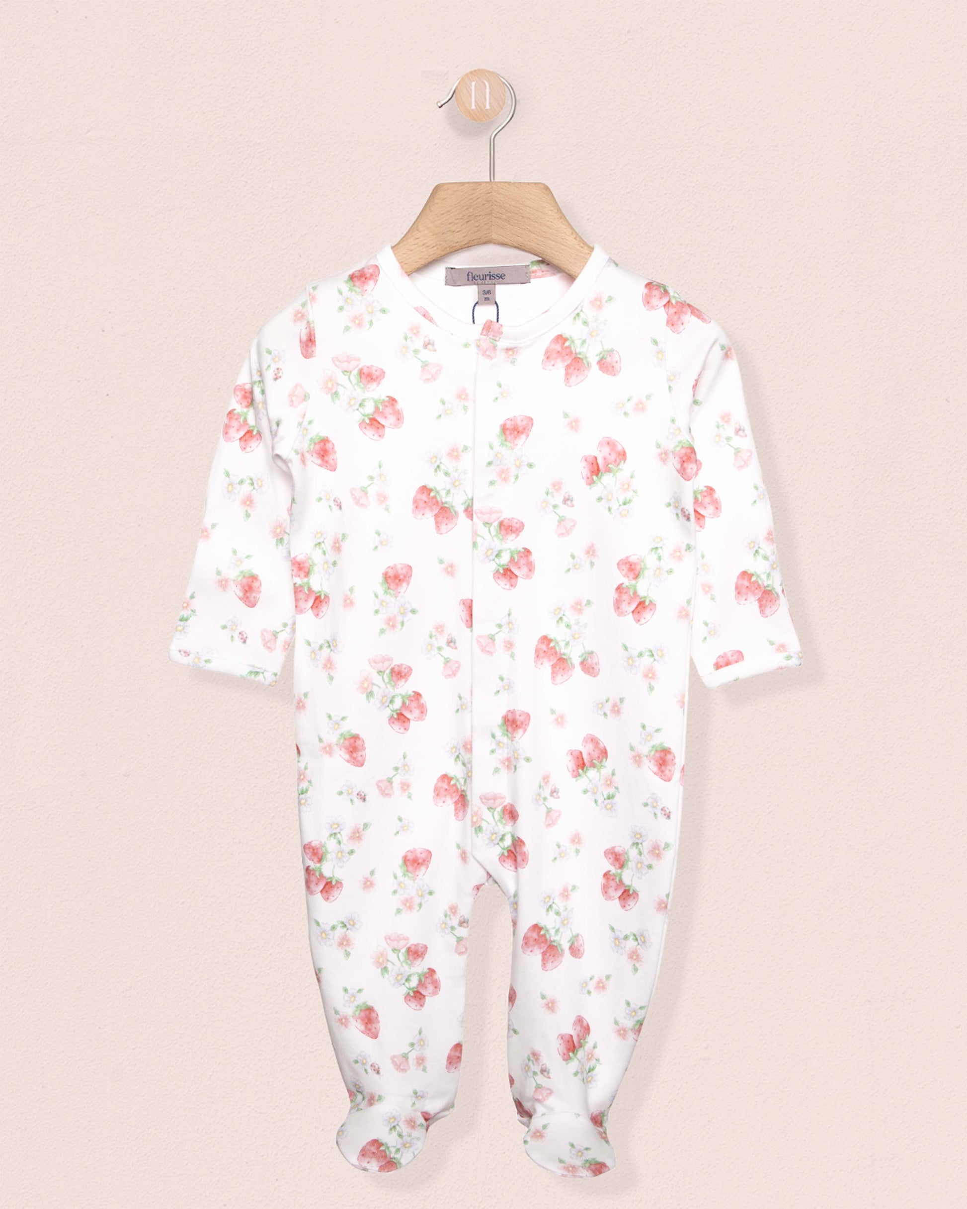 white onesie stretchie for babies with red strawberry designs, on a hanger against a peach background