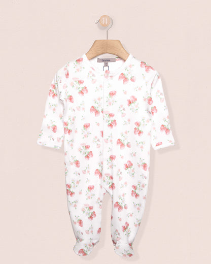 white onesie stretchie for babies with red strawberry designs, on a hanger against a peach background