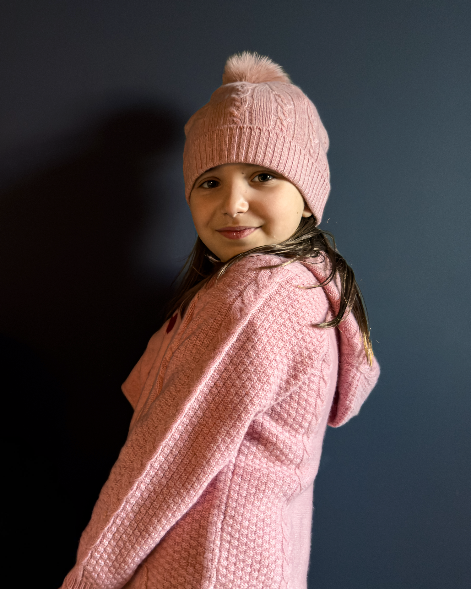 Young girl wearing a pink knit hat and sweater against a dark background