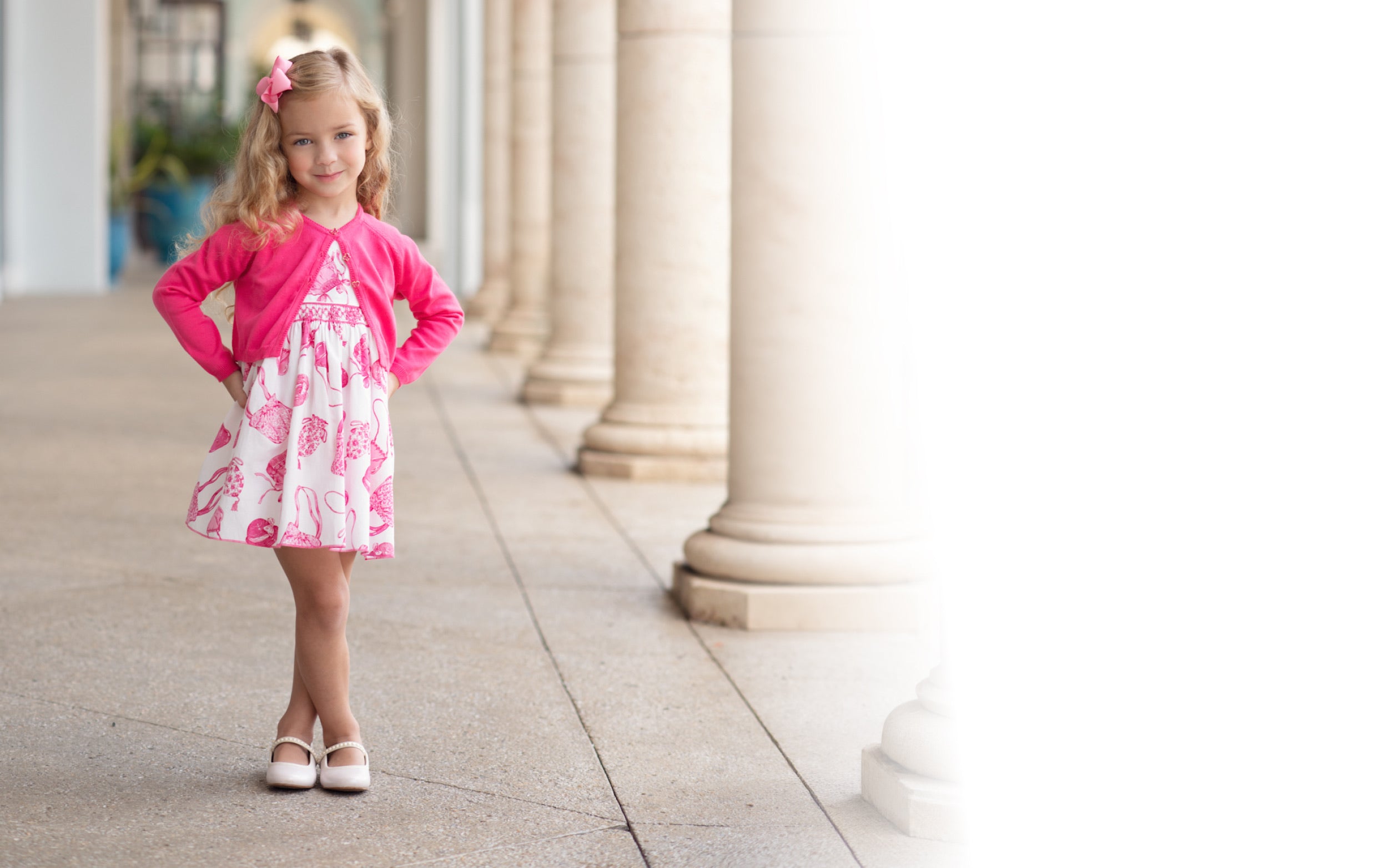 Young girl in a pink dress standing on a sidewalk with columns in the background